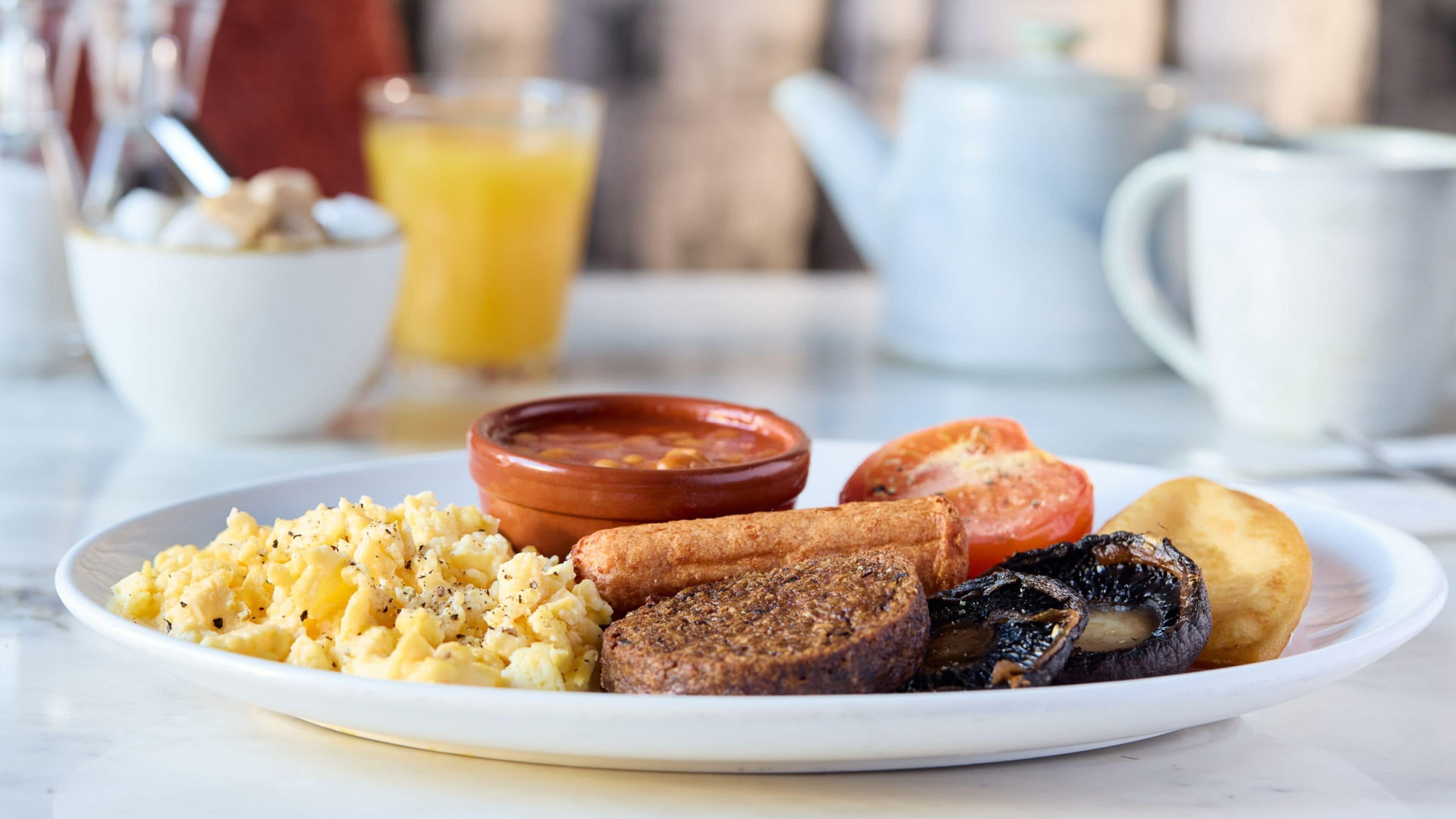 Ein Frühstücksteller mit Rührei, Würstchen, einer Tomatenscheibe und Pilzen.