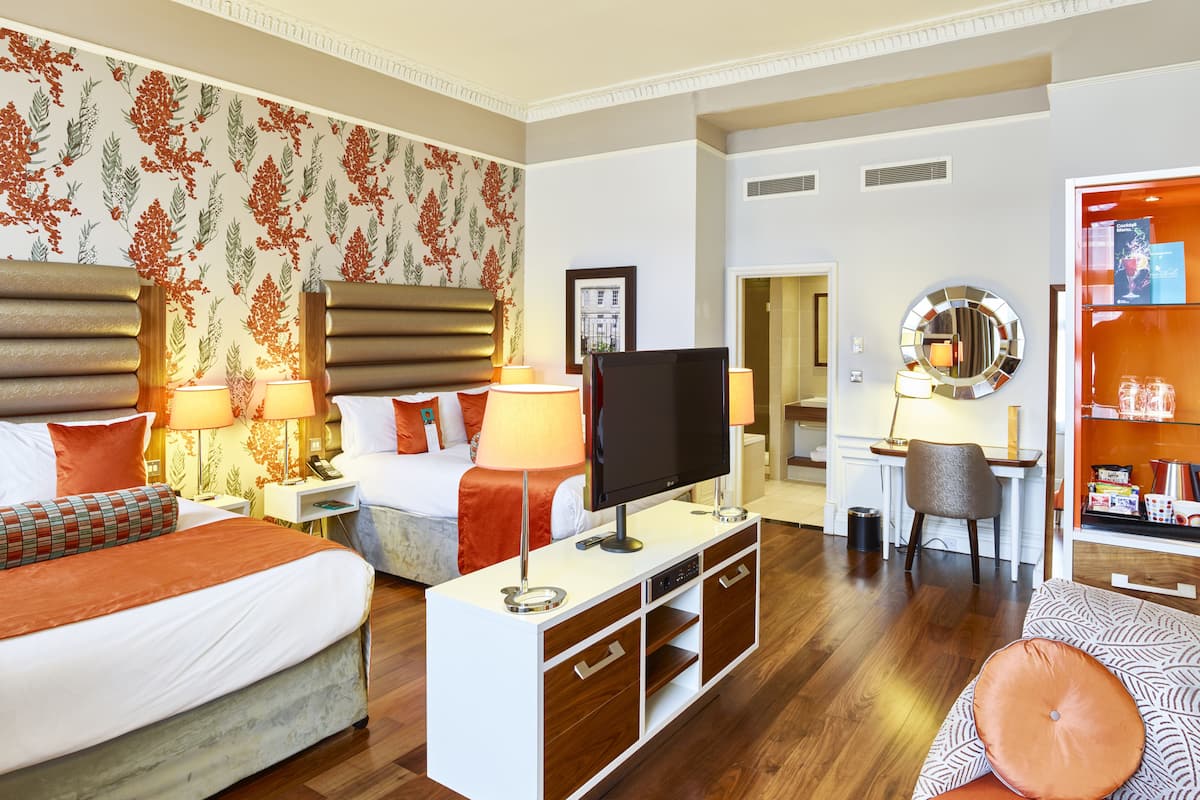 A hotel room with a bed, bedside tables, a desk, a TV, and a bathroom visible through an open door.