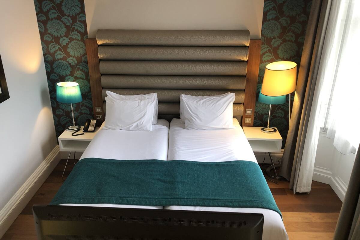 A hotel room with a large bed, two bedside tables, a headboard, and two lamps.