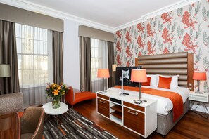 A hotel room with a large bed, two bedside tables with lamps, a desk with drawers, a chair, a small round table with a vase of flowers, and a patterned rug. - Hotel Indigo Edinburgh by IHG (Edinburgh)