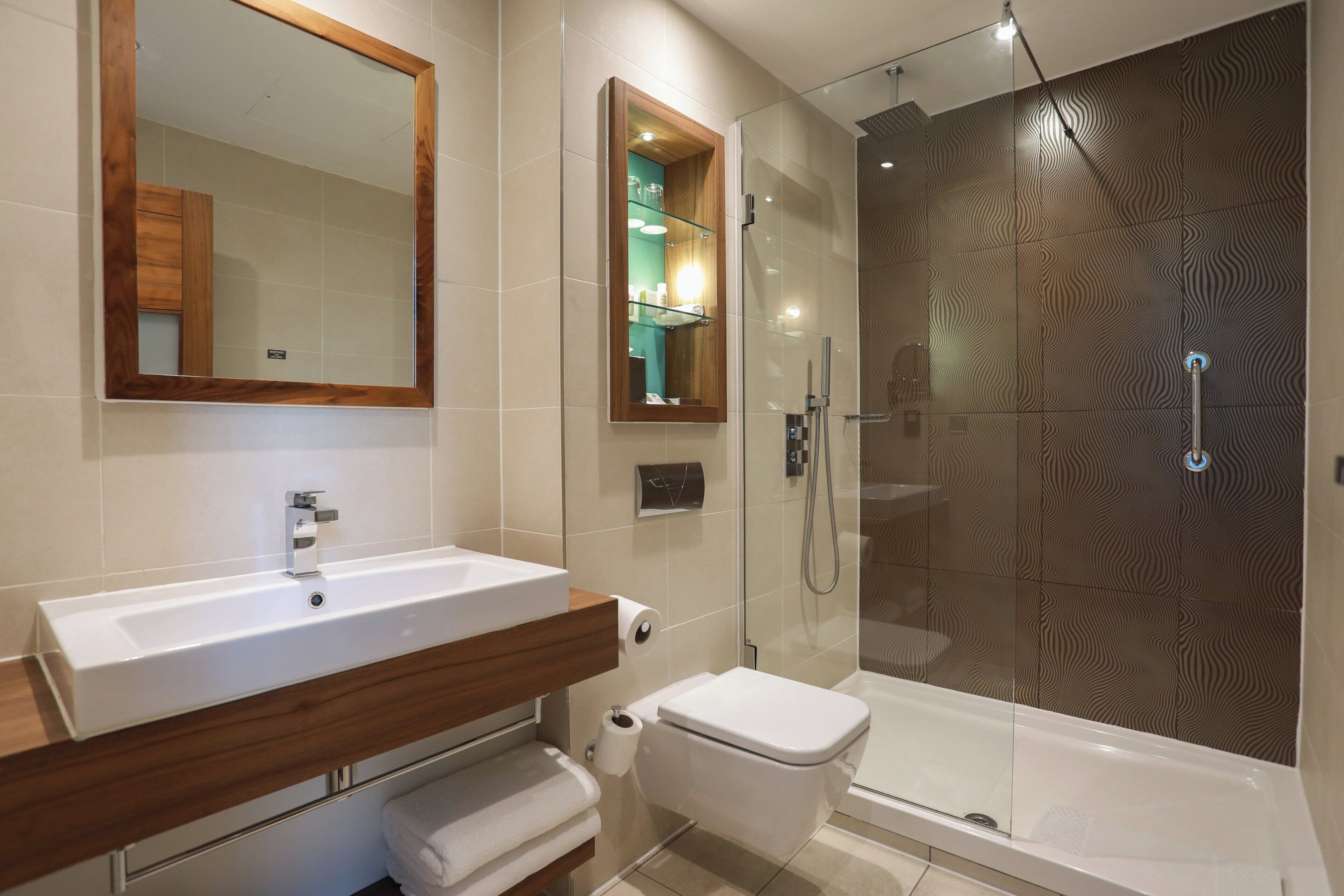 A modern bathroom with a large mirror, a sink, a toilet, and a shower enclosure.