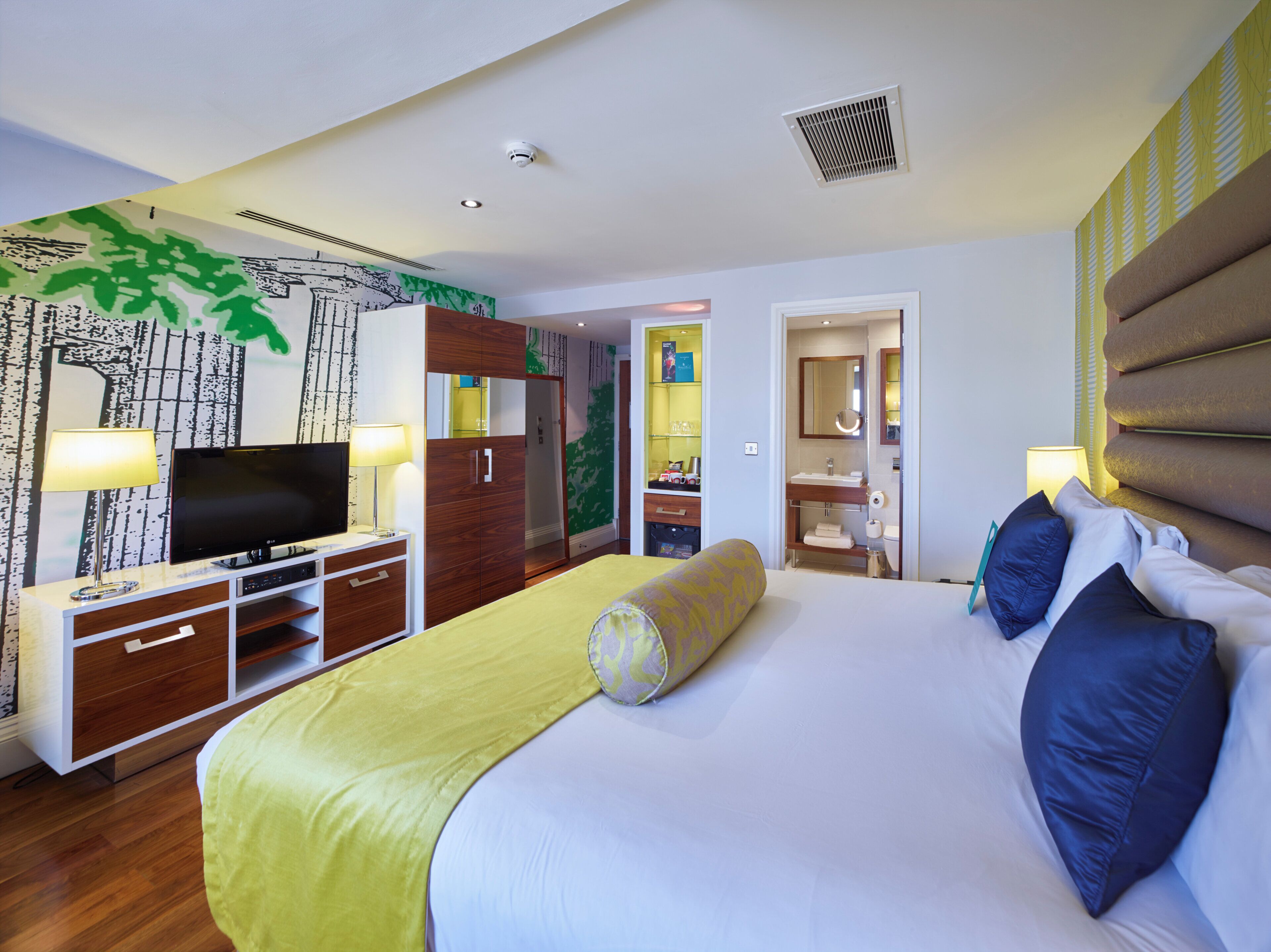 Ein Hotelzimmer mit Bett, Fernseher, Kleiderschrank und einem durch eine offene Tür einsehbaren Badezimmer.