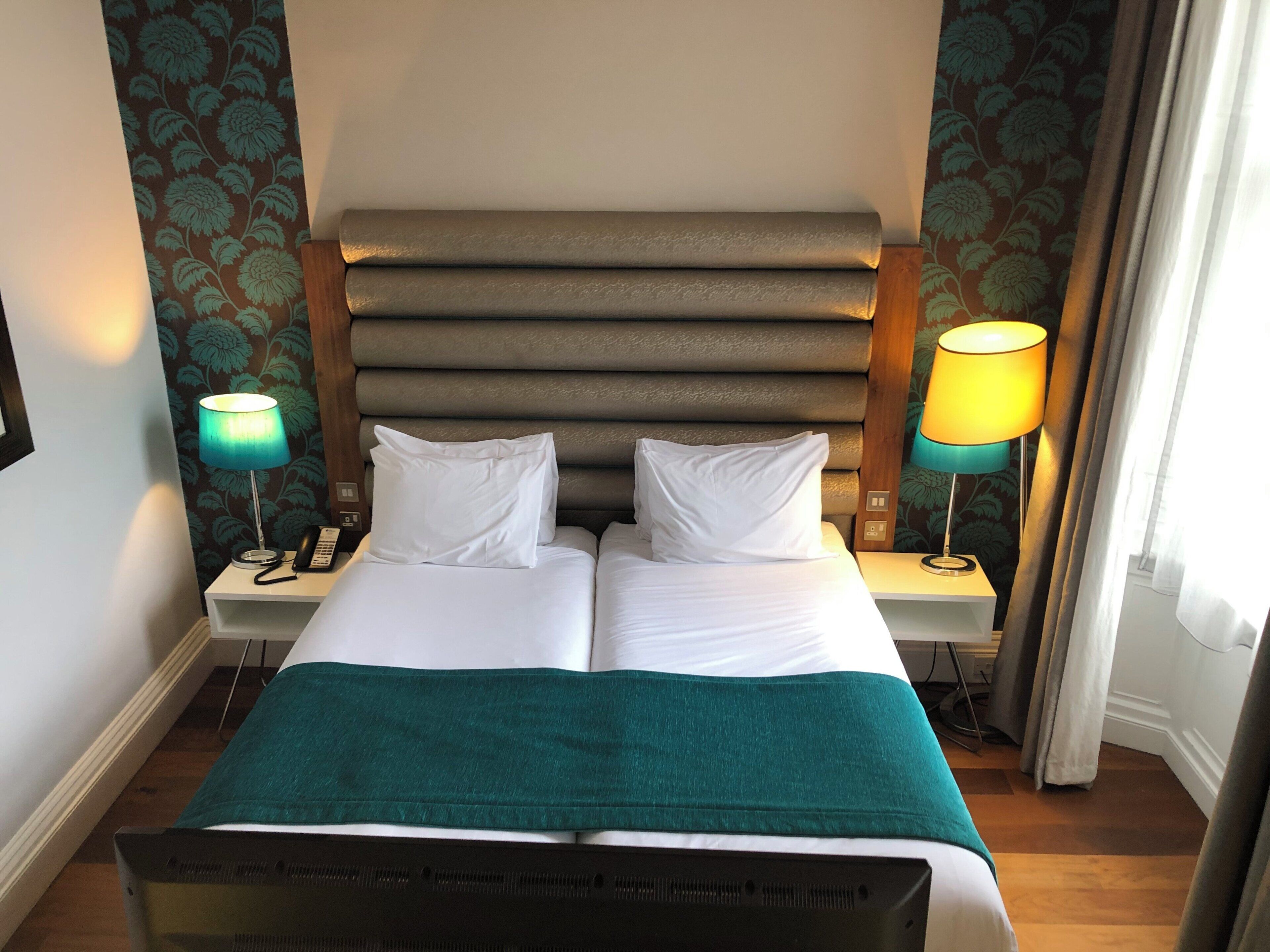 A double bed with a headboard, two bedside tables with lamps, and a green throw blanket.