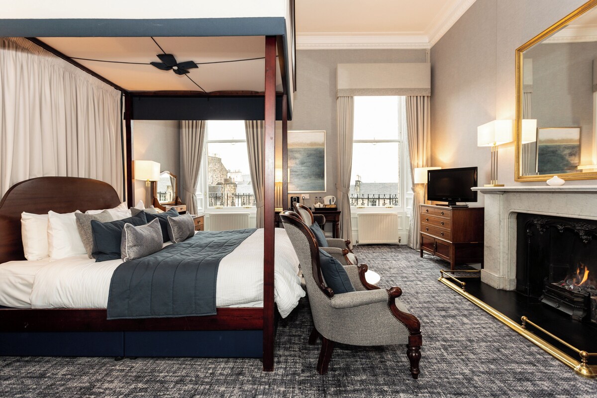 A four-poster bed with a view of the city, a fireplace, and a television in a hotel room.