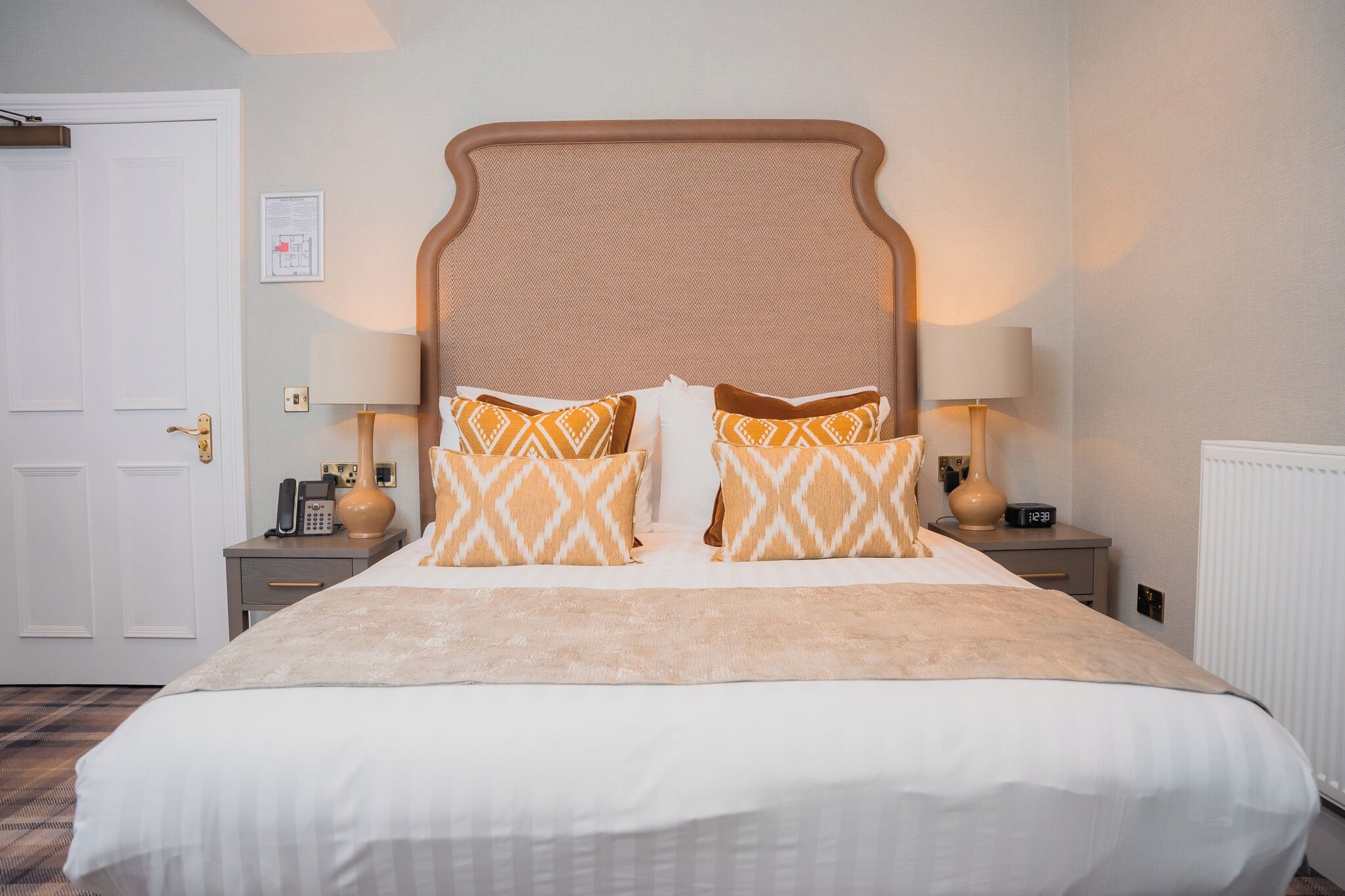 A hotel room with a large bed, two bedside tables, a nightstand, a lamp, and a wall-mounted clock.