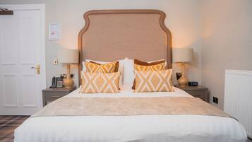 A hotel room with a large bed, two bedside tables, a nightstand, a lamp, and a wall-mounted clock.