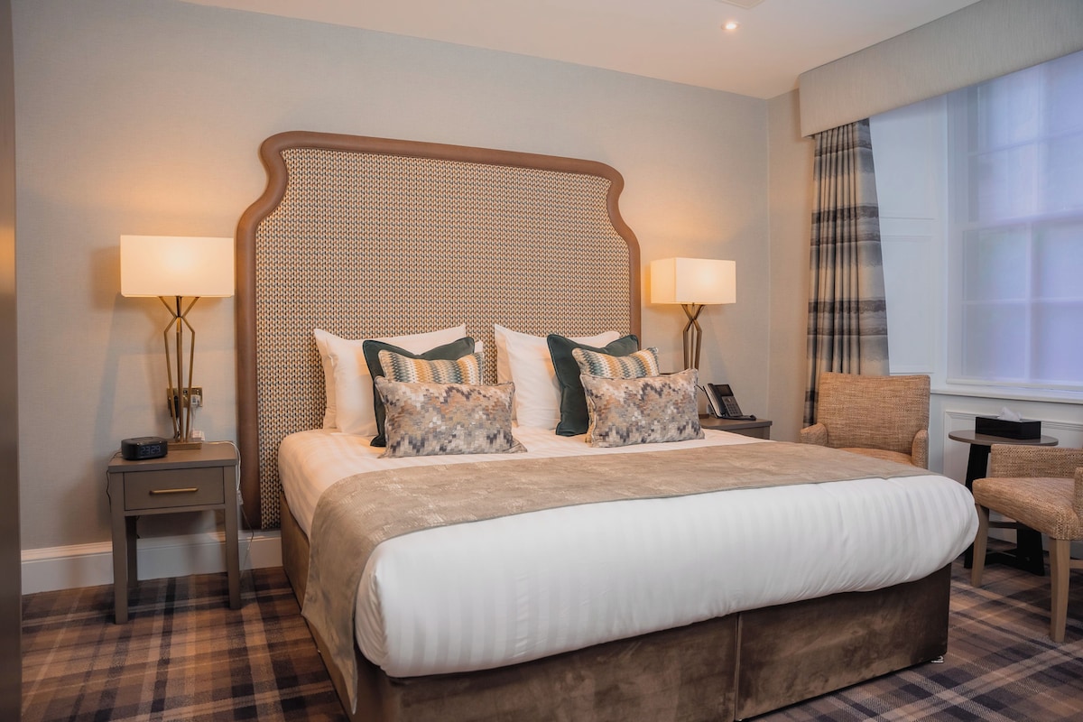 A hotel room with a large bed, two bedside tables, a chair, and a window with curtains.