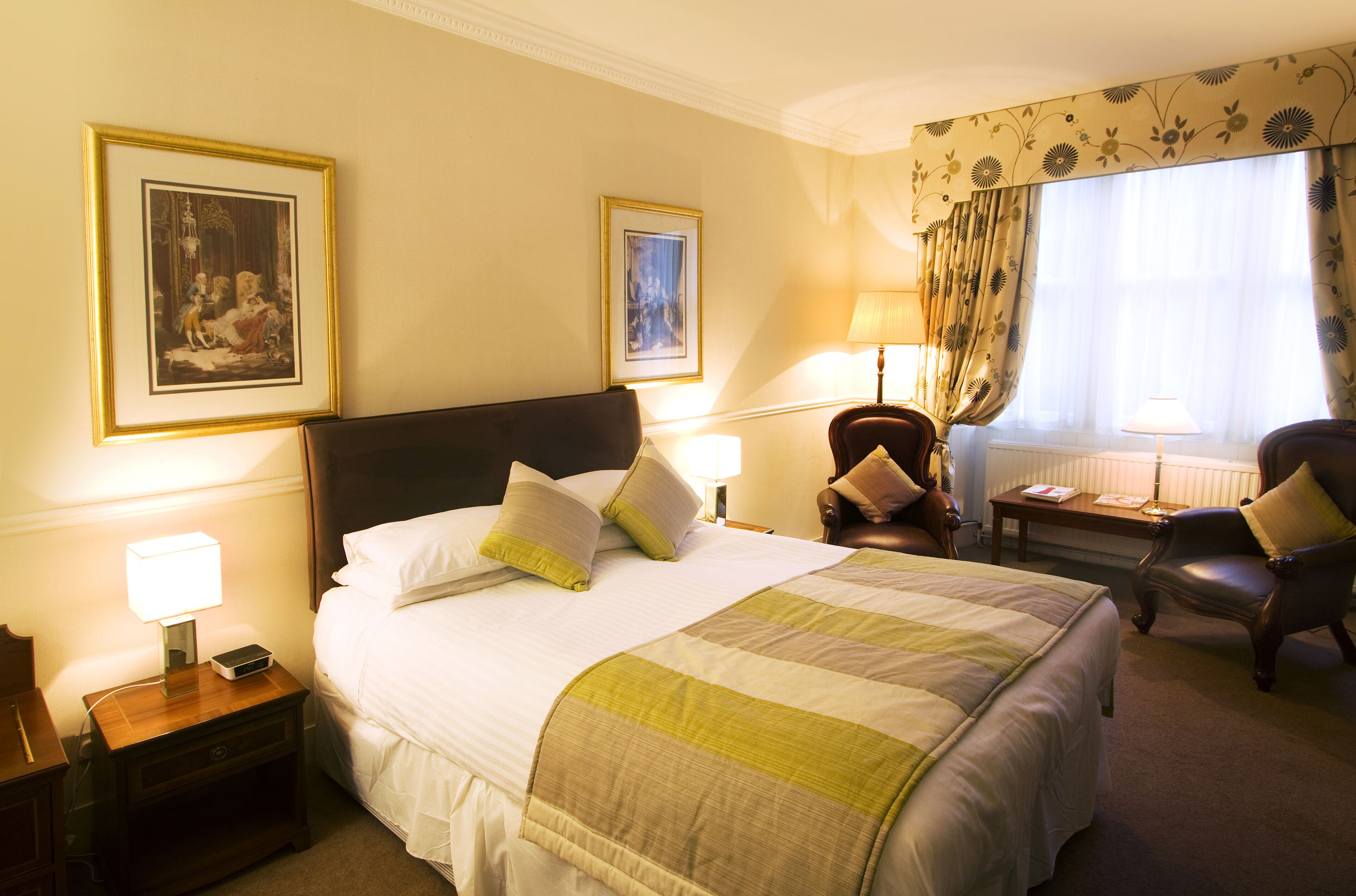 A hotel room with a large bed, two bedside tables with lamps, a chair, and two framed pictures on the wall.