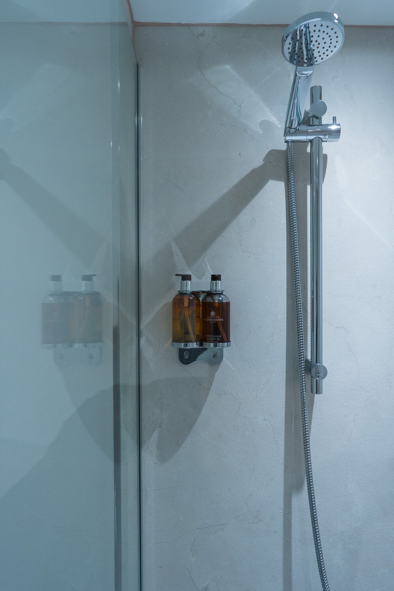 Une douche fermée par des parois en verre, dotée d’un pommeau de douche à main et d’un distributeur de savon à main.
