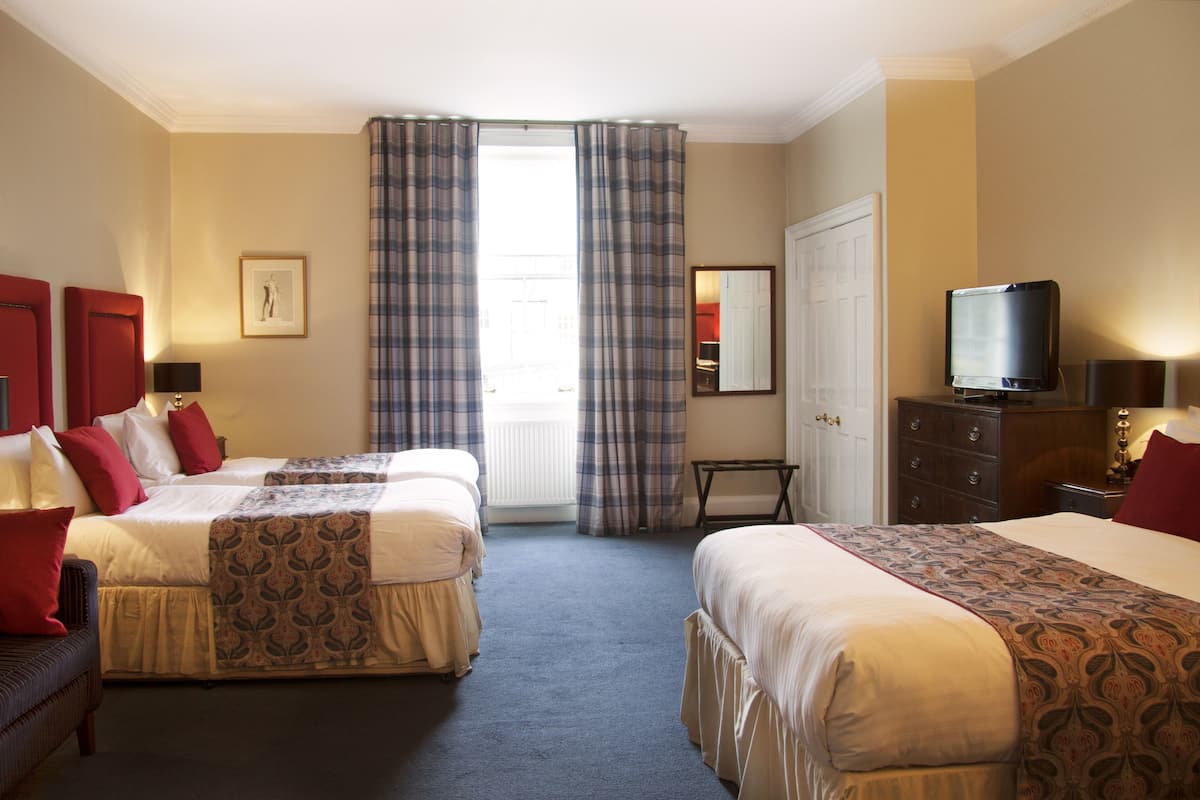 A hotel room with two beds, a television, a dresser, and a window with curtains.