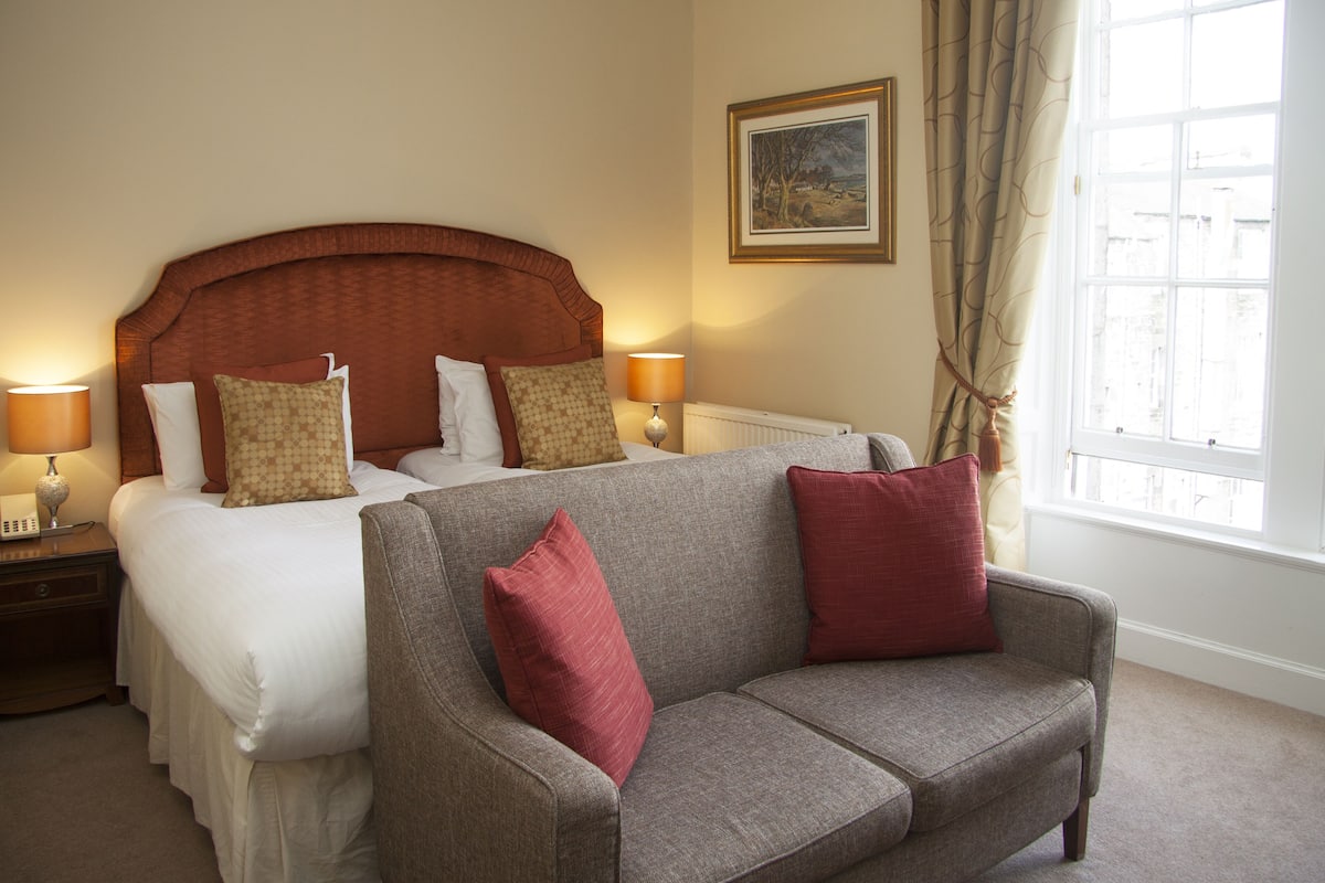 A hotel room with a large bed, a grey sofa, and two bedside tables with lamps.