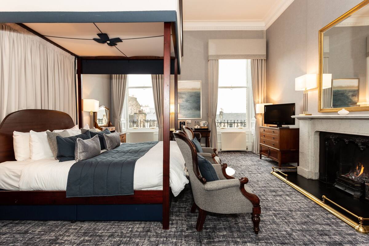 A four-poster bed with a view of the city, a fireplace, and a television in a hotel room.