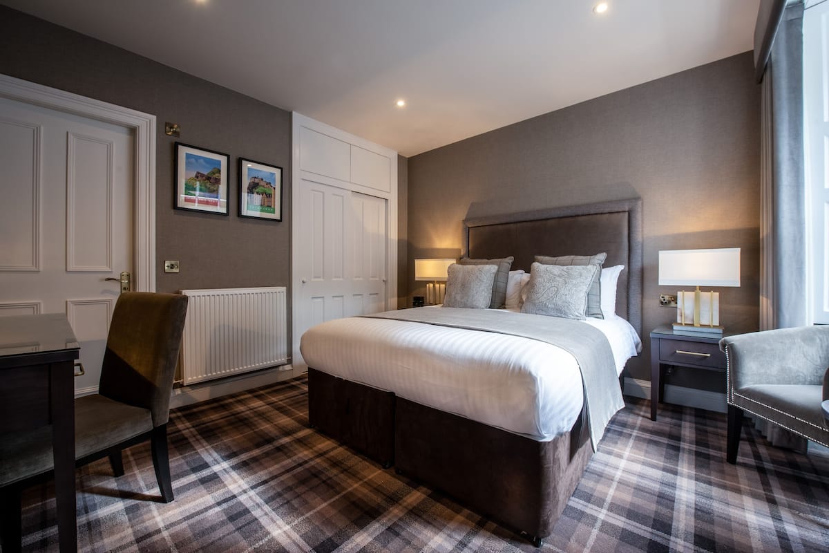 A bedroom with a large bed, a chair, a desk, and a radiator.