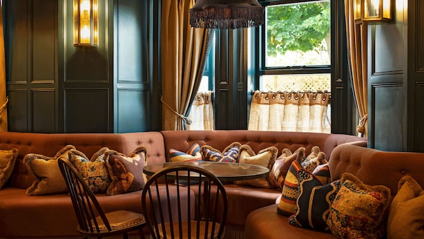 A cozy room with a tufted sofa, patterned cushions, a wooden chair, and a window with curtains. - Beadnell Towers (Chathill)