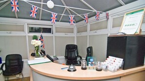 A reception desk with flags, a black office chair, a coffee machine, and a framed certificate. - Skylark B&B (Hounslow)