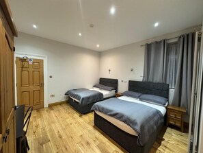 Une chambre avec deux lits, un plancher en bois, une porte et une table de chevet.