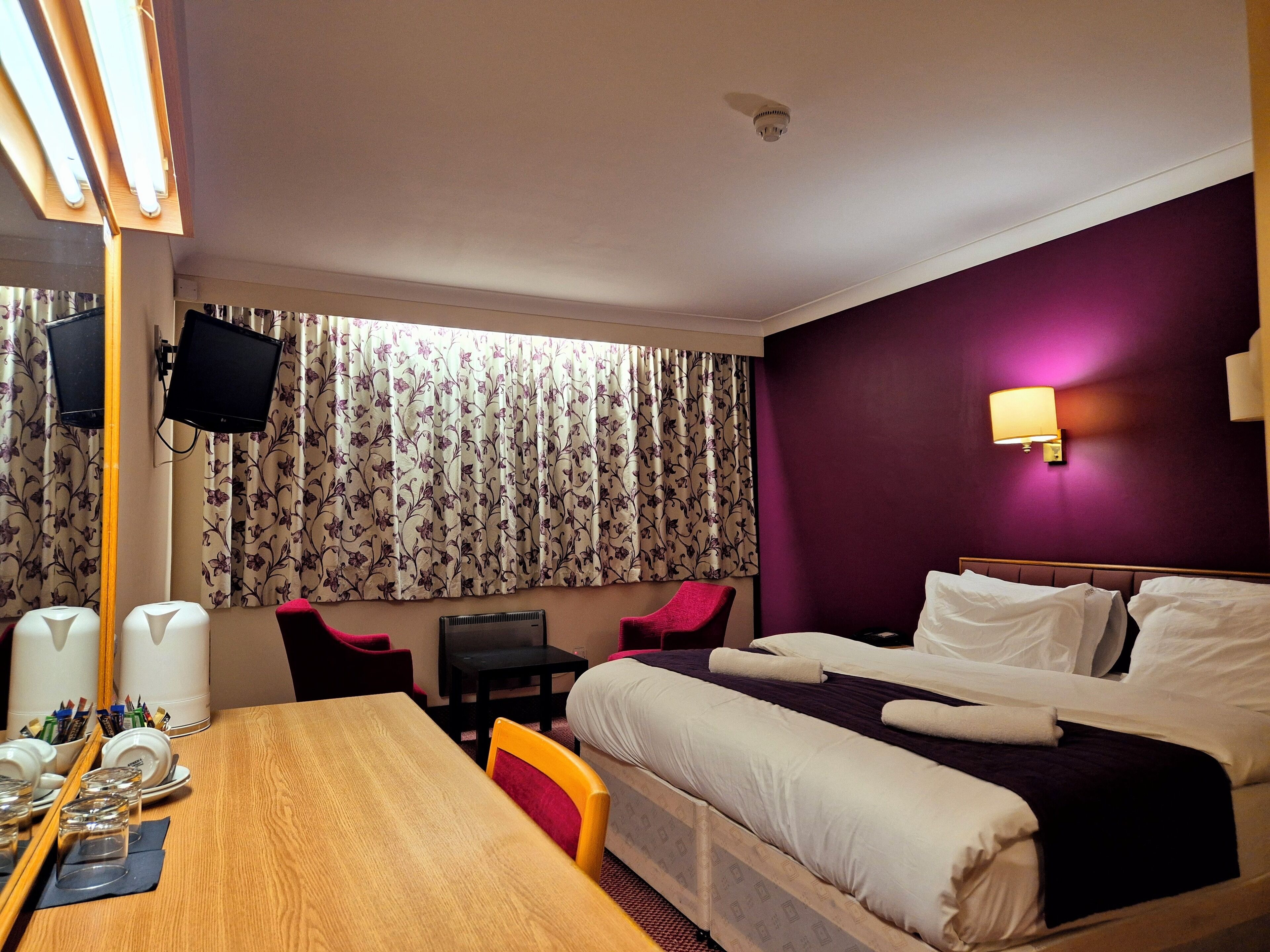 A hotel room with a bed, a desk with chairs, a television, and a window with curtains.