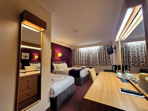 Habitación de hotel con una cama grande, una cama más pequeña, un escritorio con cafetera, televisor y espejo.