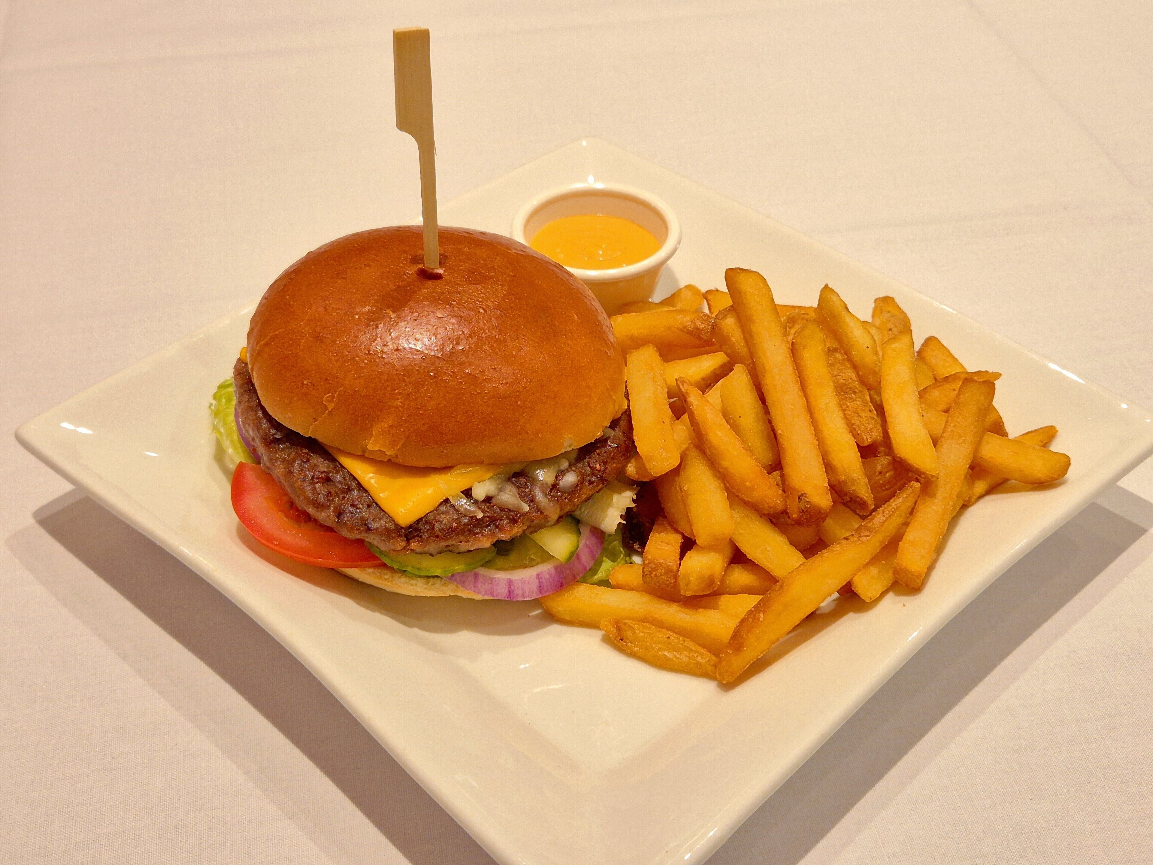 Un plato con una hamburguesa, papas fritas y un pequeño recipiente de salsa.