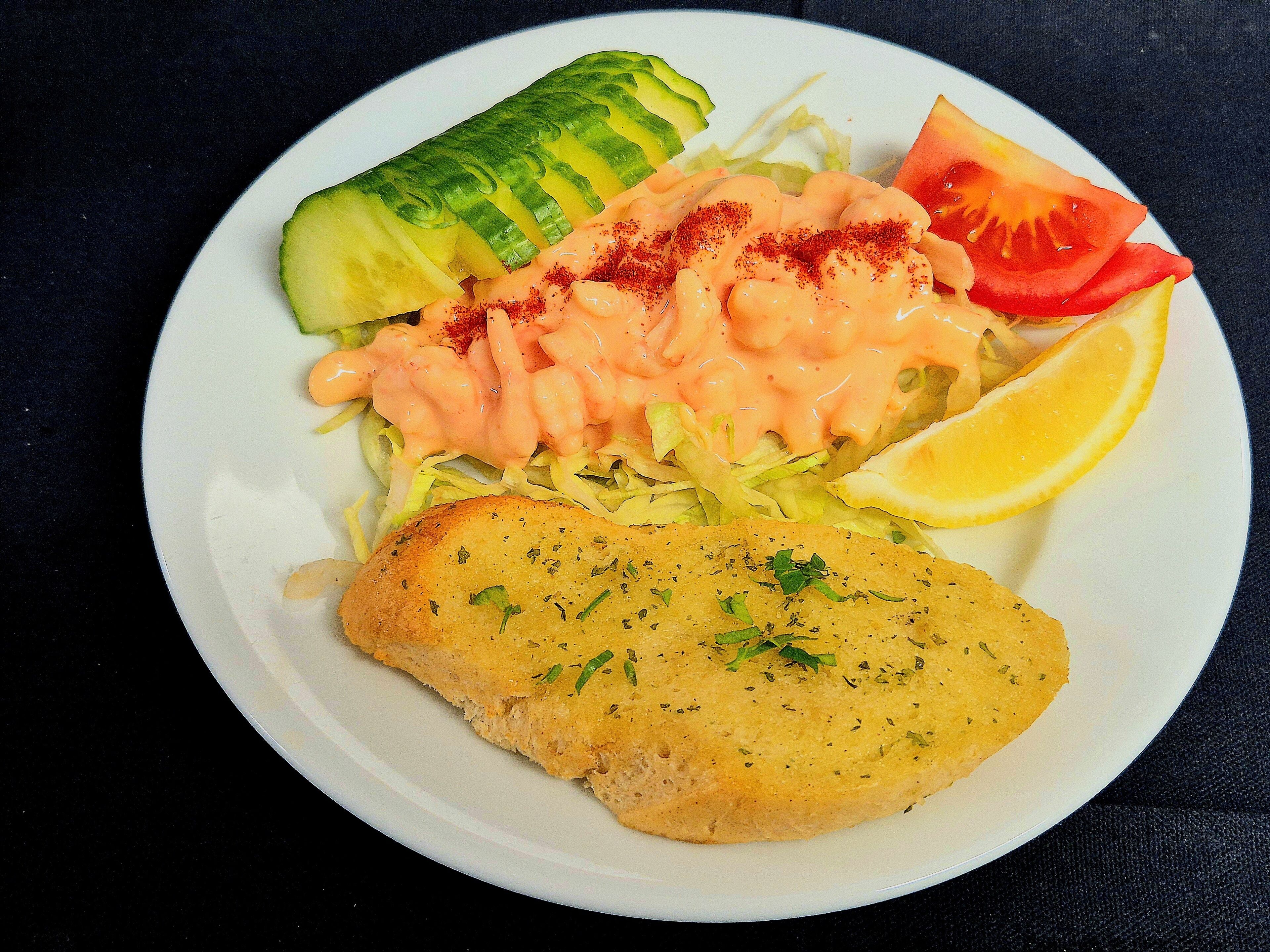 Ein Teller mit einem panierten Schnitzel, Gurkenscheiben, Tomaten und einer cremigen Soße.
