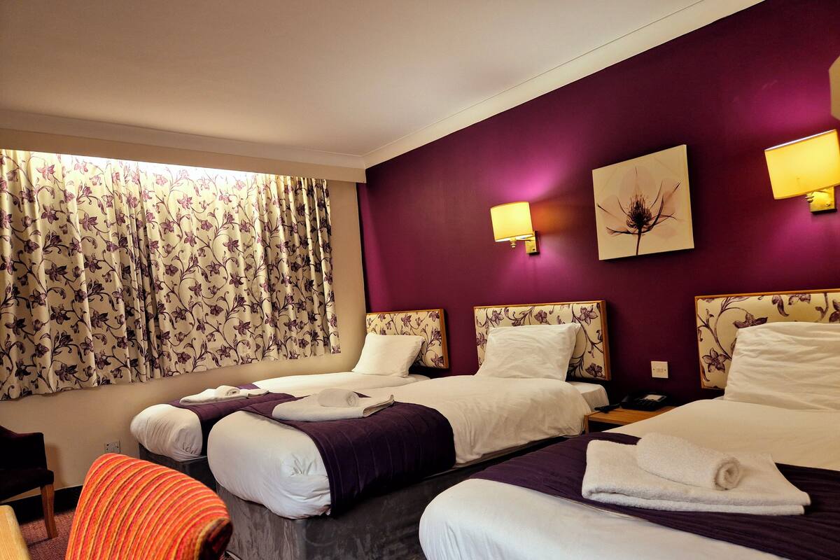 A hotel room with two beds, a desk, a chair, and a window with curtains.