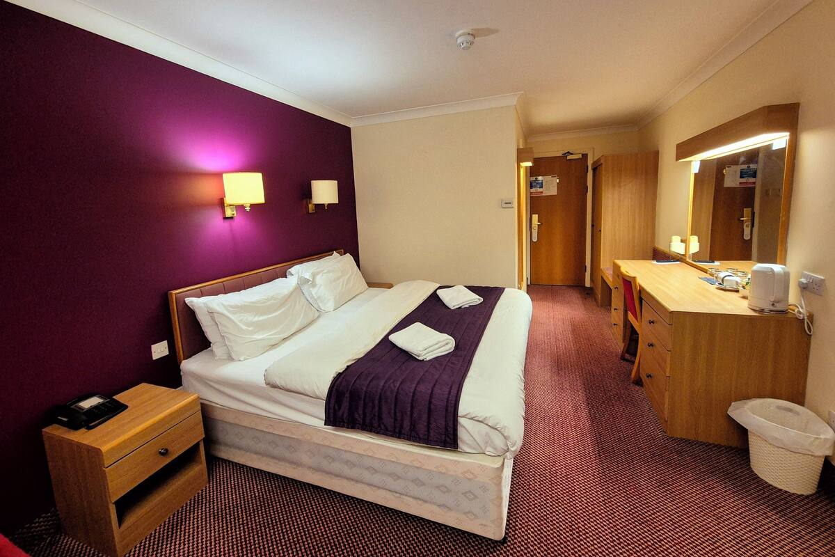 A hotel room with a bed, bedside table, and a bathroom with a sink and mirror.