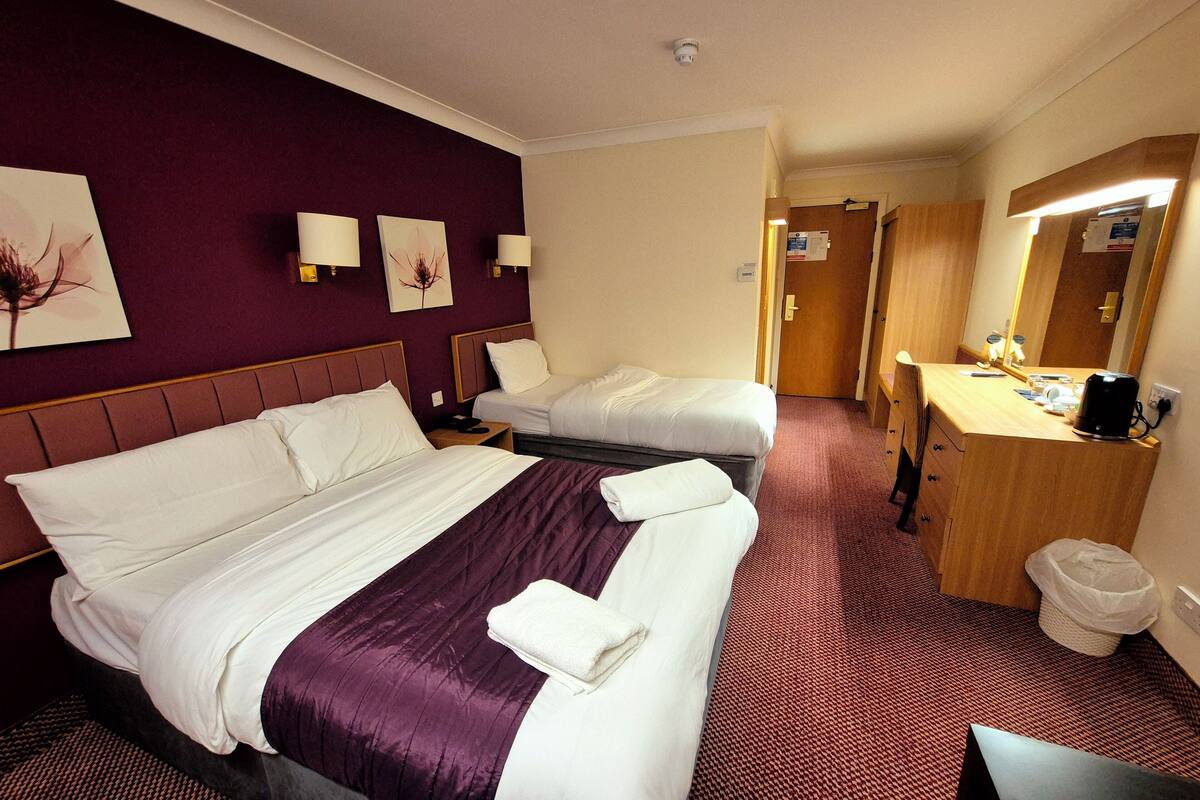 A hotel room with two beds, a desk, a mirror, and a trash bin.