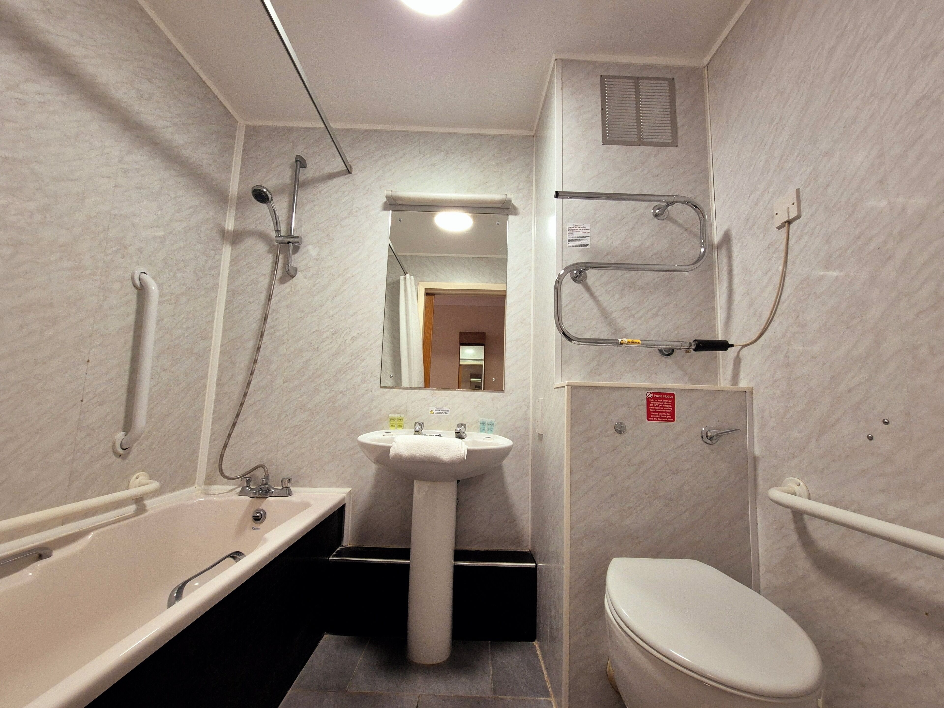 A bathroom with a bathtub, sink, and toilet, equipped with grab bars and a shower chair.