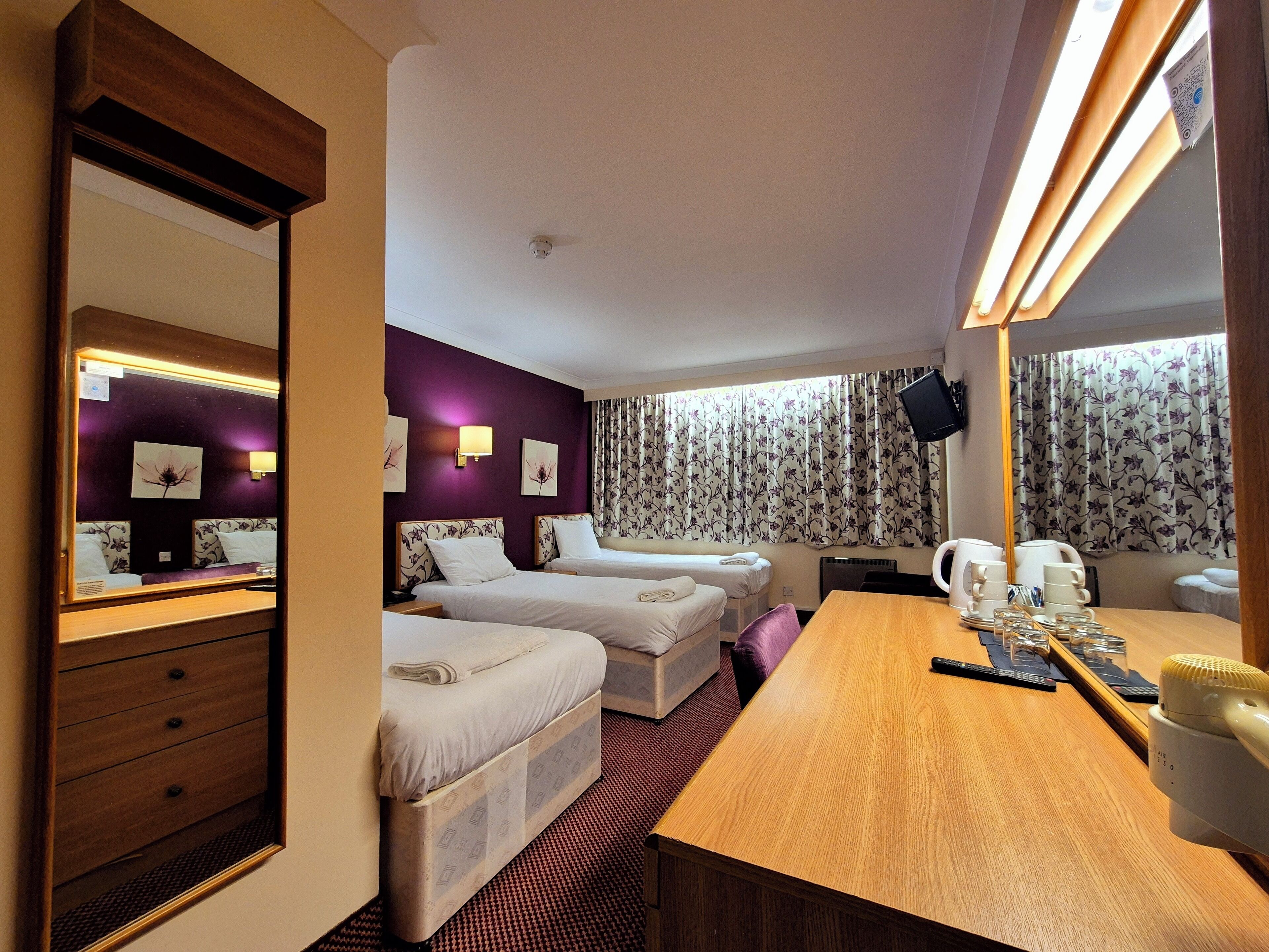 A hotel room with two beds, a wooden desk, a mirror, and a television.