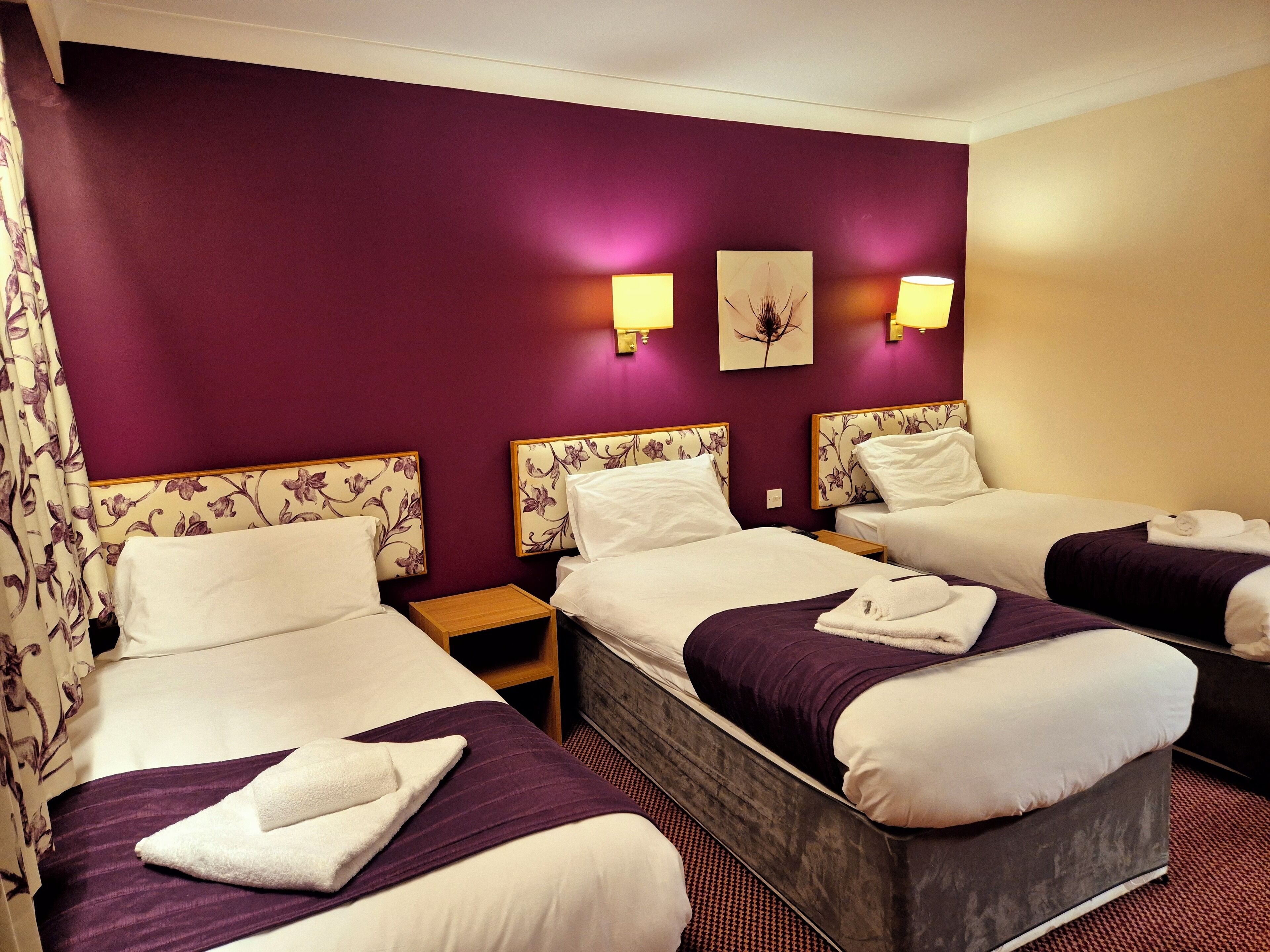 A hotel room with three beds, purple walls, and floral headboards.