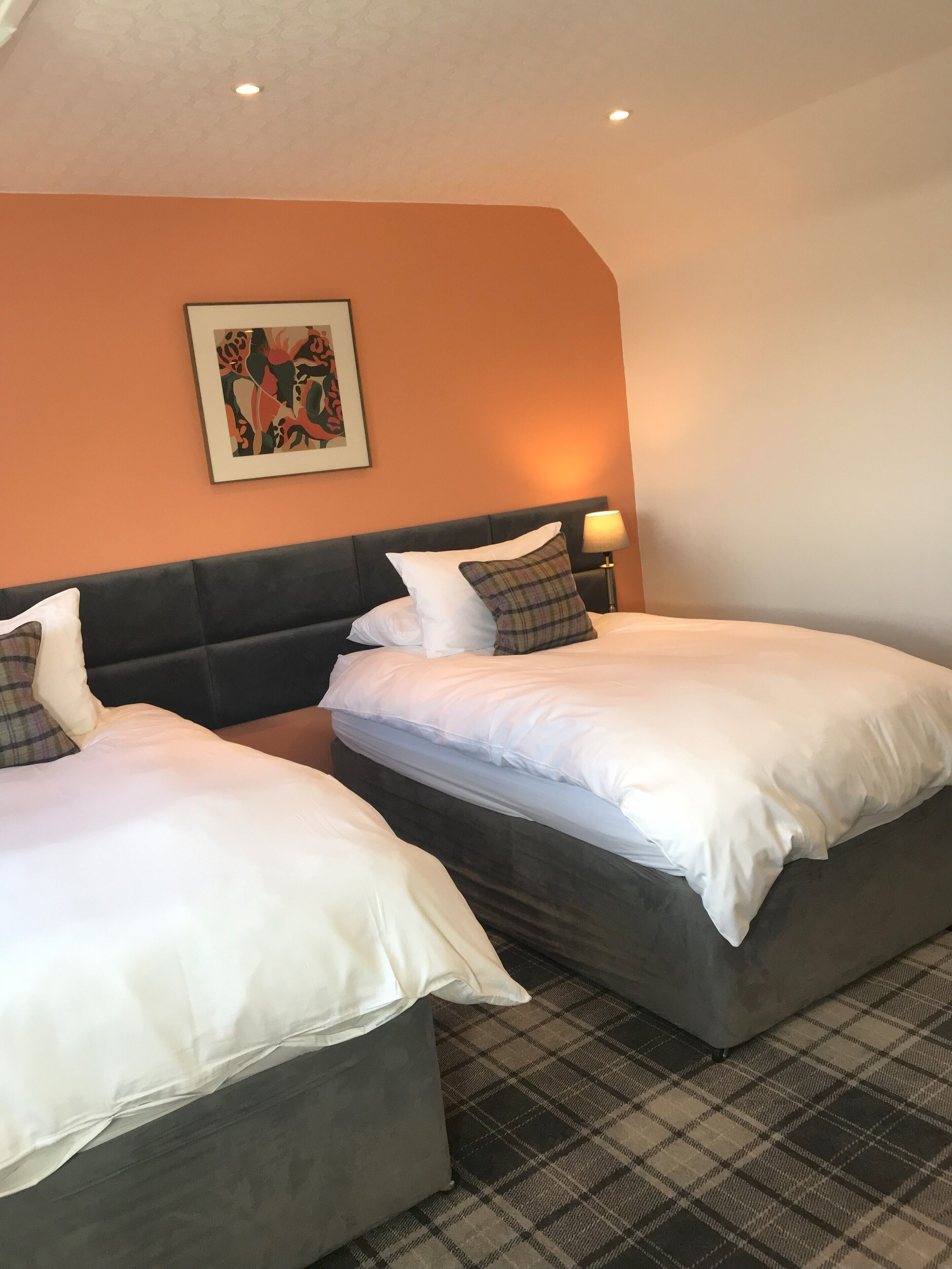 A hotel room with two beds, a headboard, a wall-mounted picture, and a floor lamp.