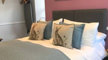Una cama bien hecha con colcha acolchada y almohadas con diseño de conejos, cabecera y una obra de arte colgada en la pared.