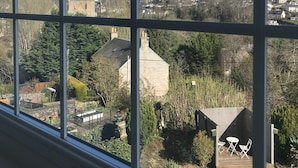 A view through a window with a grid pattern, featuring a rural landscape with houses, trees, and a distant building. - Meadhon House (Jedburgh)