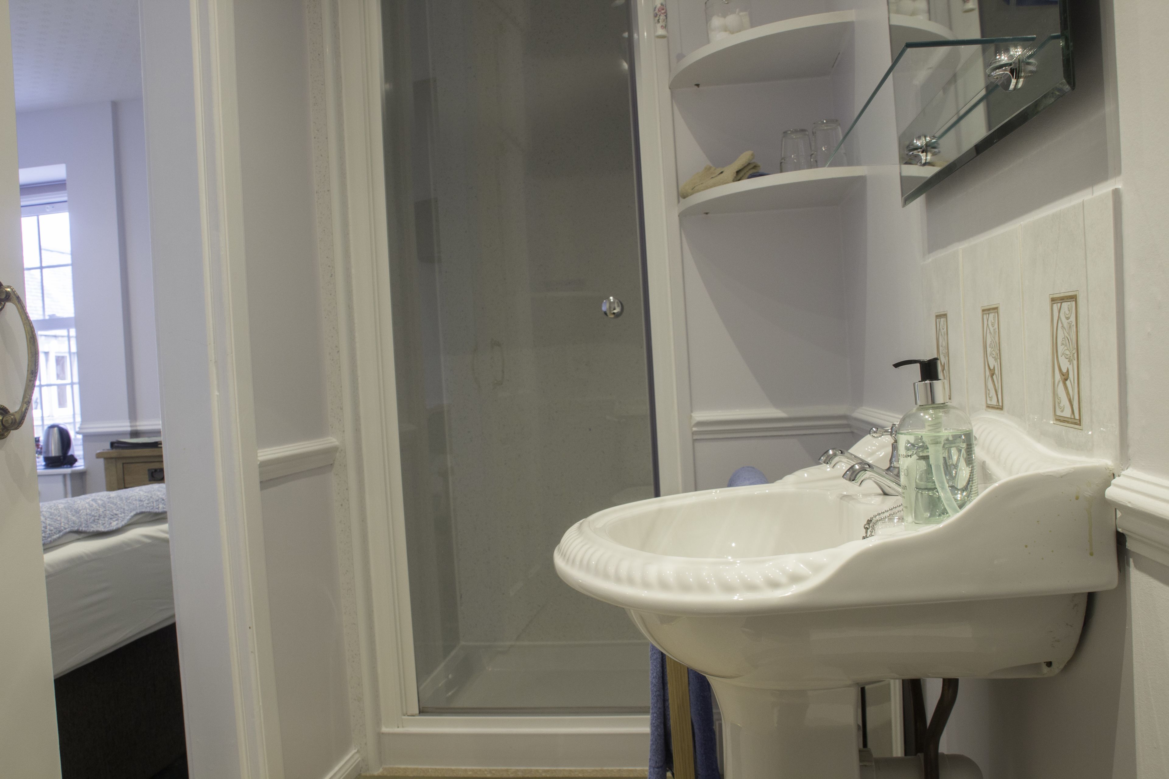 A bathroom with a white sink, a glass shower enclosure, and a shelf with toiletries.