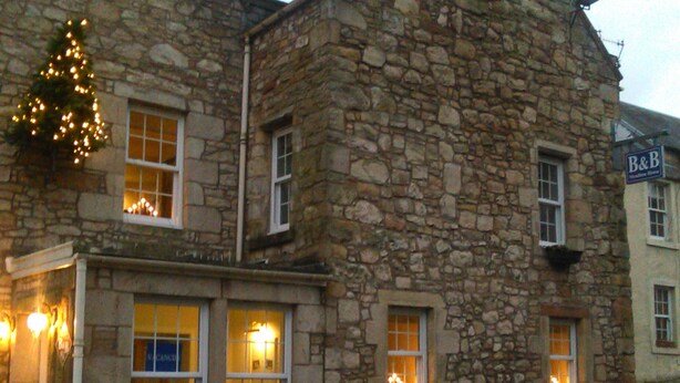 A stone building with a B&B sign, multiple windows with lights, and a Christmas tree with lights. - Meadhon House (Jedburgh)