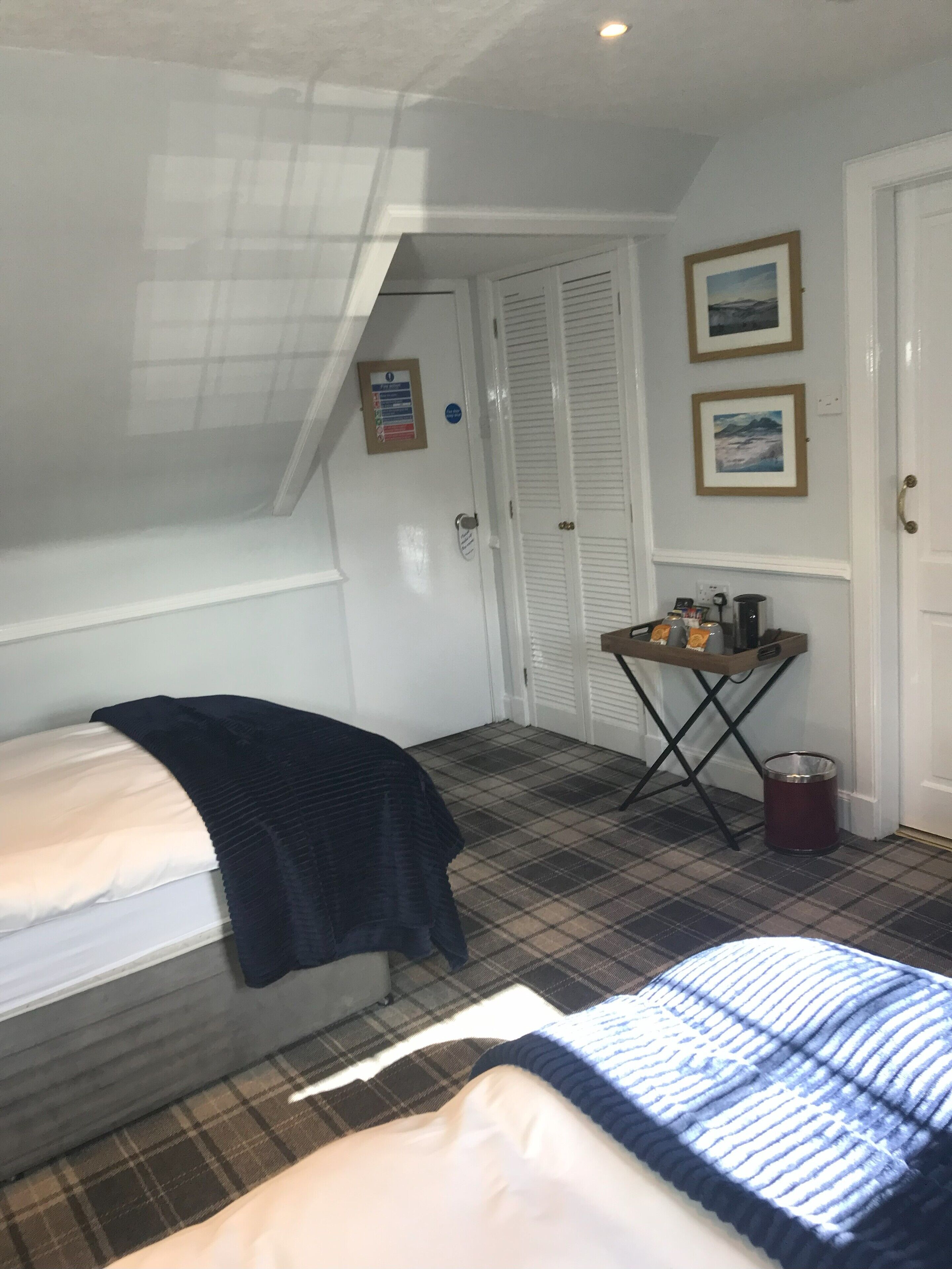 Una habitación pequeña y funcional con cama, una mesita y una silla, una puerta y una ventana.