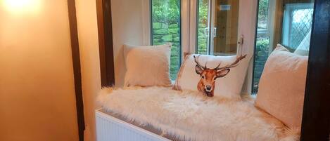 Una habitación acogedora con un ventanal grande, un radiador y una cama mullida de piel blanca.