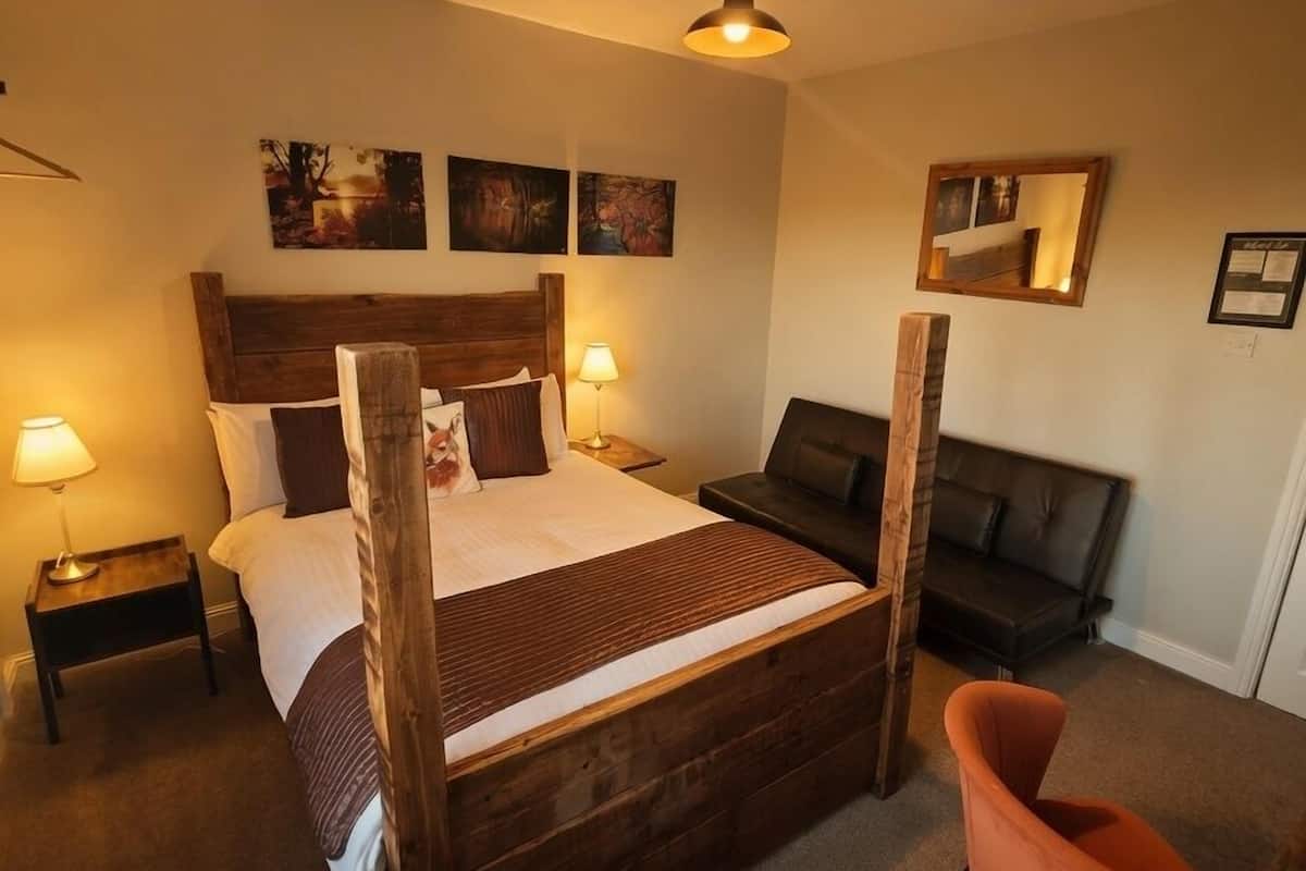 Un dormitorio con una cama de madera con dosel, dos lámparas de noche, un sofá negro, un espejo y obras de arte en las paredes.