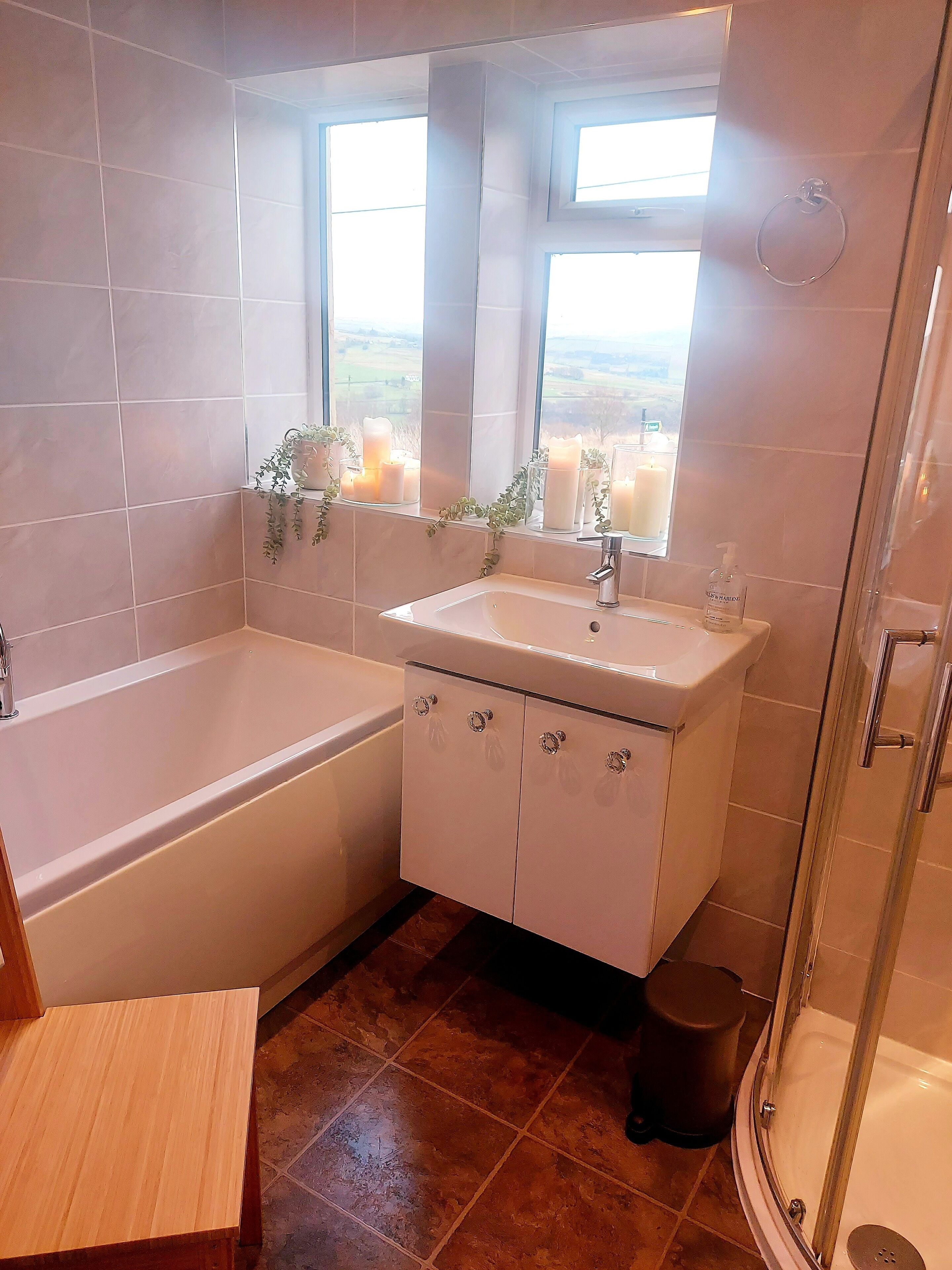 Een badkamer met een bad, een wastafel met spiegel en een raam met kaarsen.