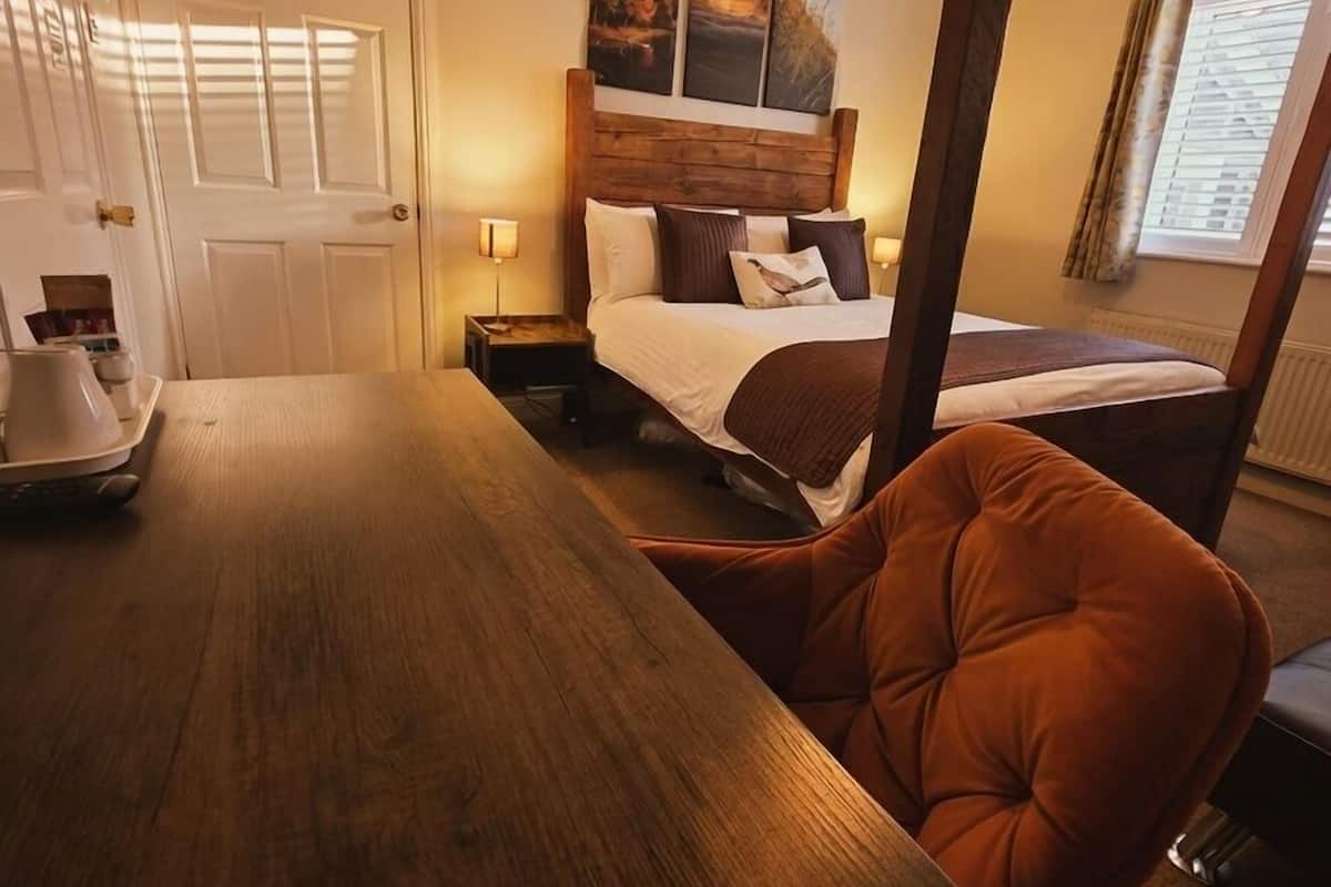 Una habitación de hotel con una cama de madera, una mesita de noche, una silla y un escritorio.