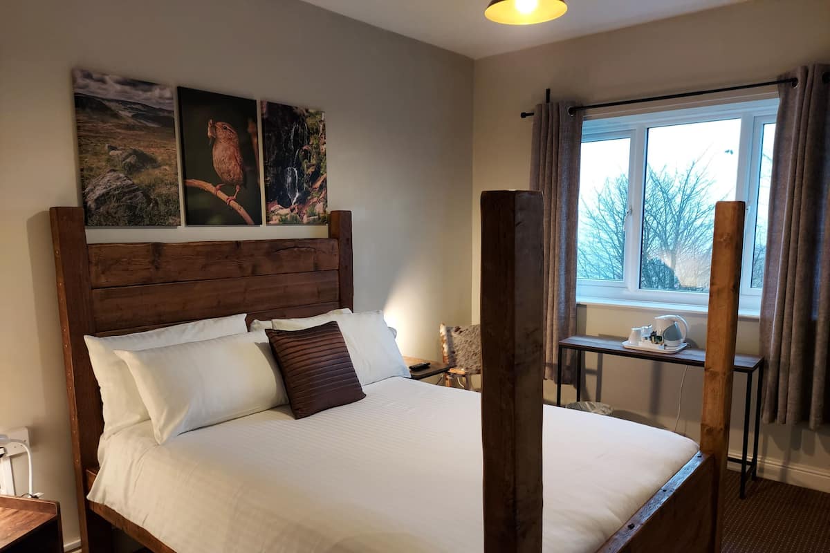 Una cama con dosel con ropa de cama blanca y marrón, un cabecero de madera y una ventana con cortinas.