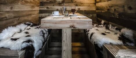 A wooden cabin interior with a central table set for two, flanked by fur-covered benches.
