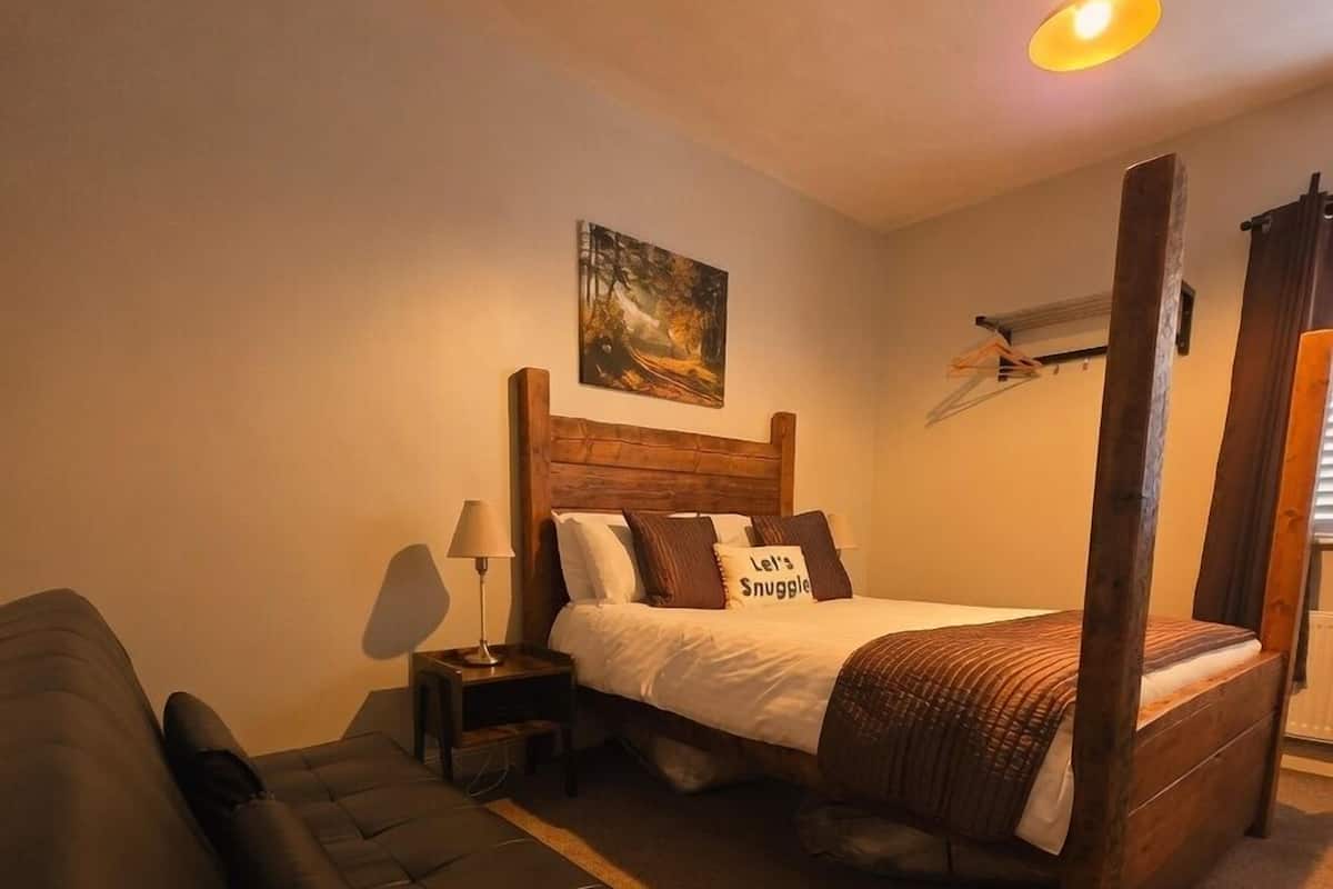 Un dormitorio con una cama con dosel, una mesita de noche con lámpara, un cuadro en la pared y un sofá de cuero oscuro.