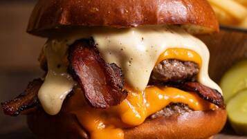Hamburguesa con tocino y queso sobre pan, acompañada de papas fritas y un pepinillo.