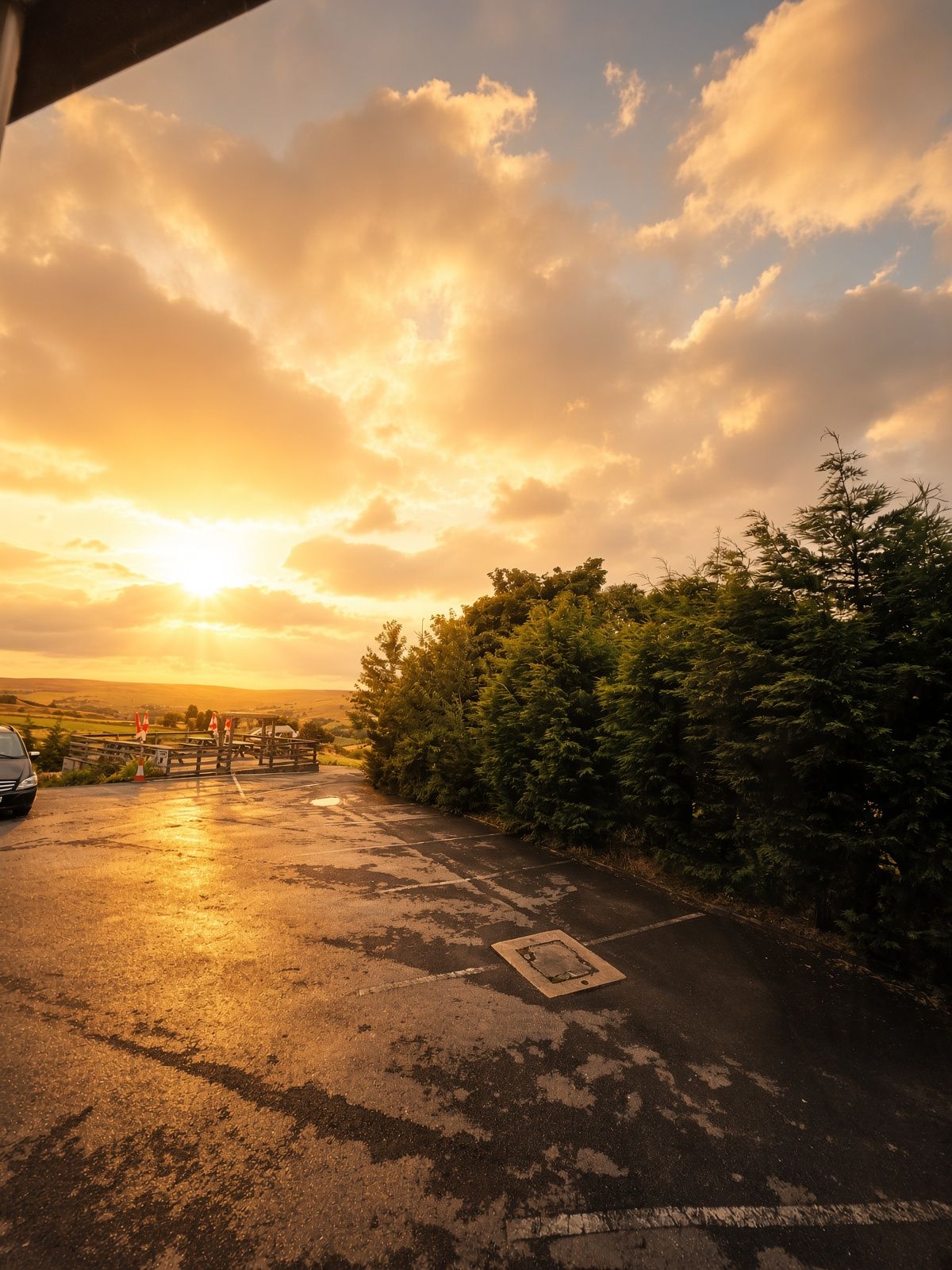 A parking area with a car, trees, and a sunset in the background.