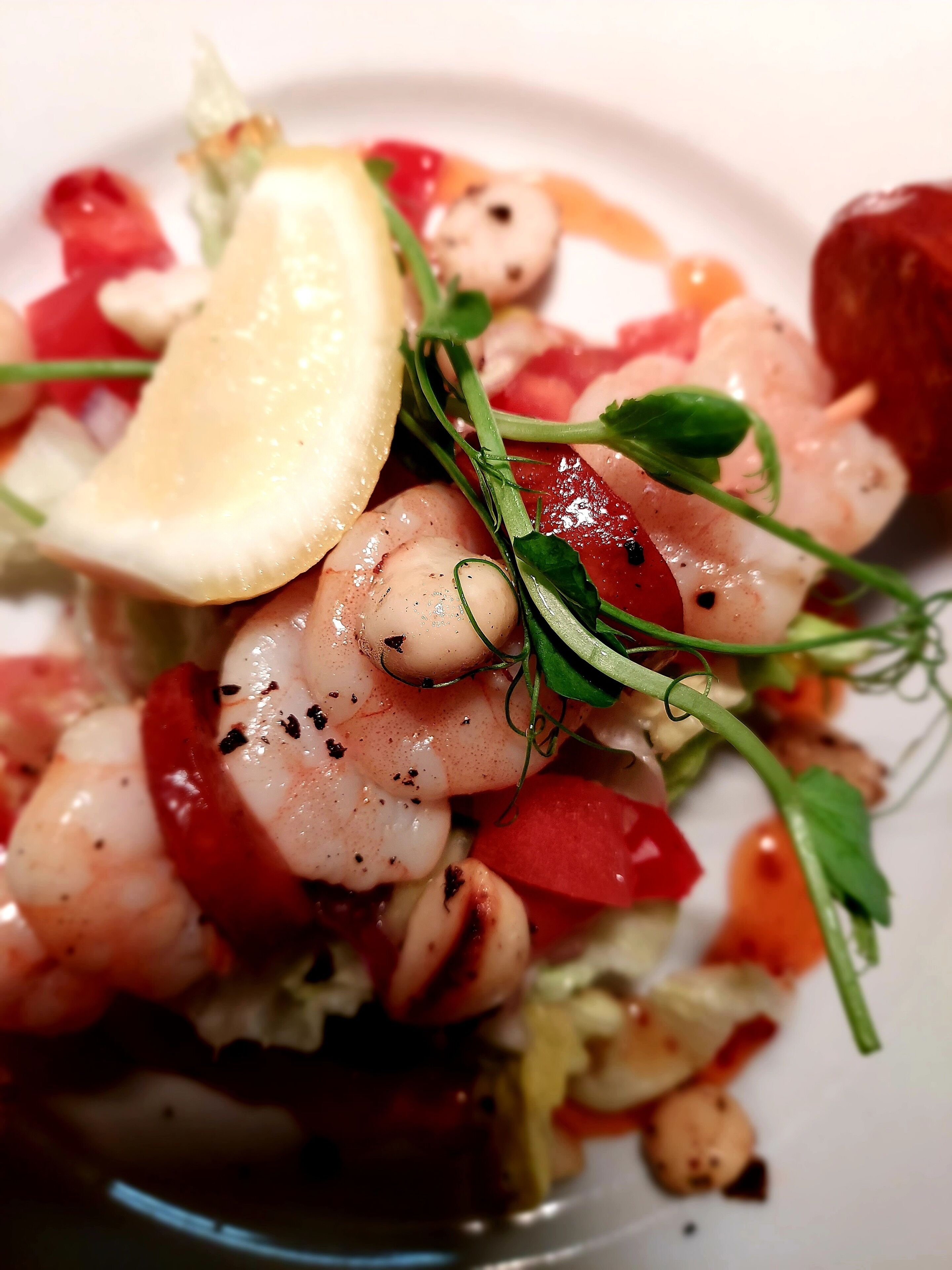 A plate of food with shrimp, tomatoes, and a lemon wedge.