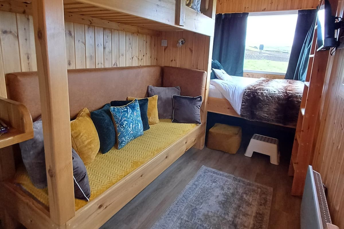 Interior acogedor de una cabaña con literas, una cama baja y un pequeño rincón de descanso.