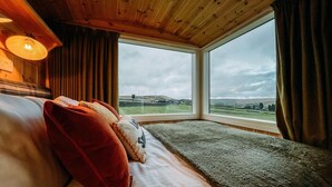 Una habitación con una cama, un ventanal con vistas a un paisaje y techo de madera.