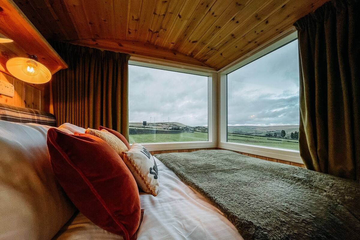 Una habitación con una cama, un ventanal con vistas a un paisaje y techo de madera.