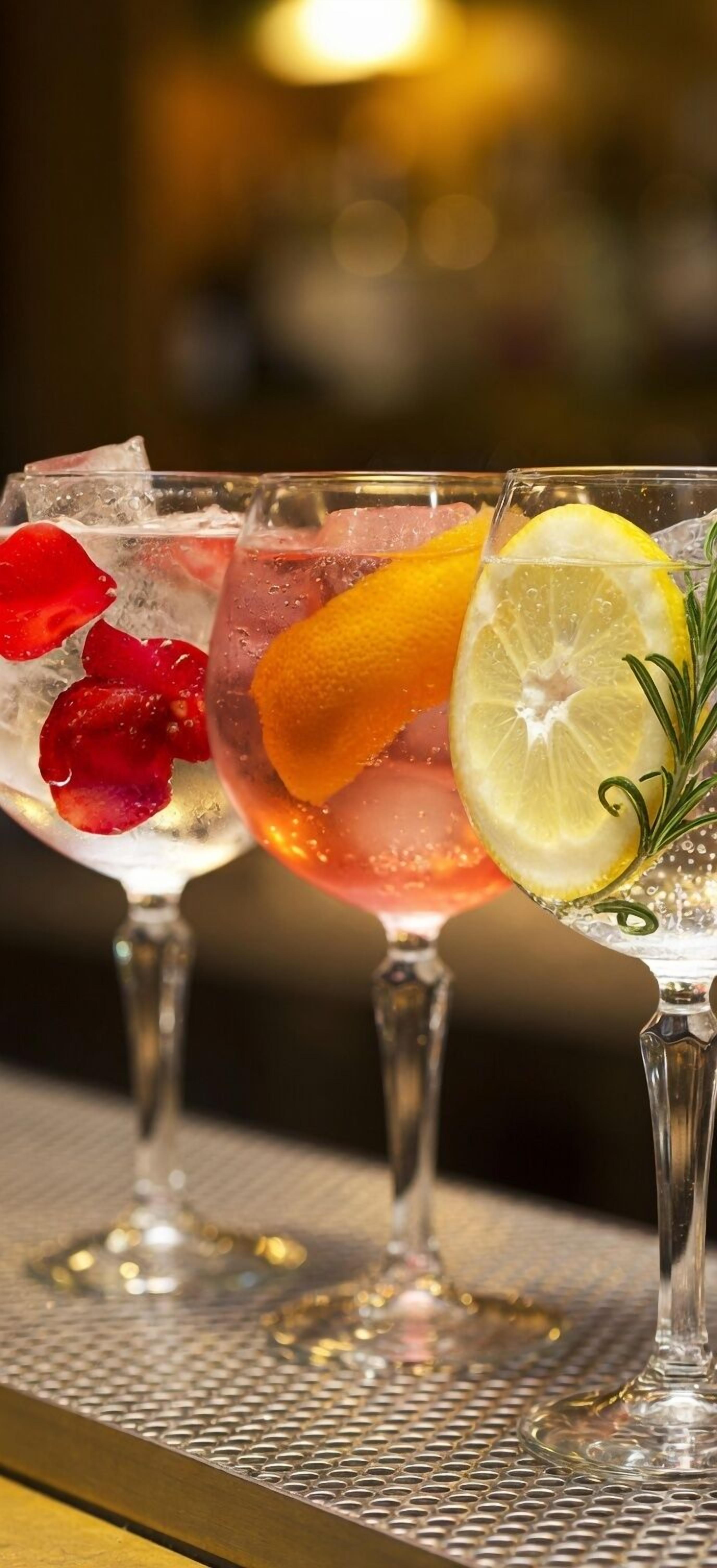 Two glasses of a cocktail with ice, garnished with a slice of orange and a sprig of rosemary.